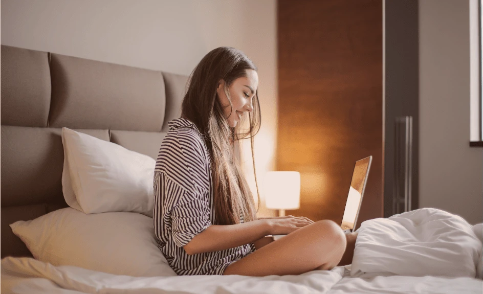 kvinne sitter på seng på hotellrom med pc i fanget