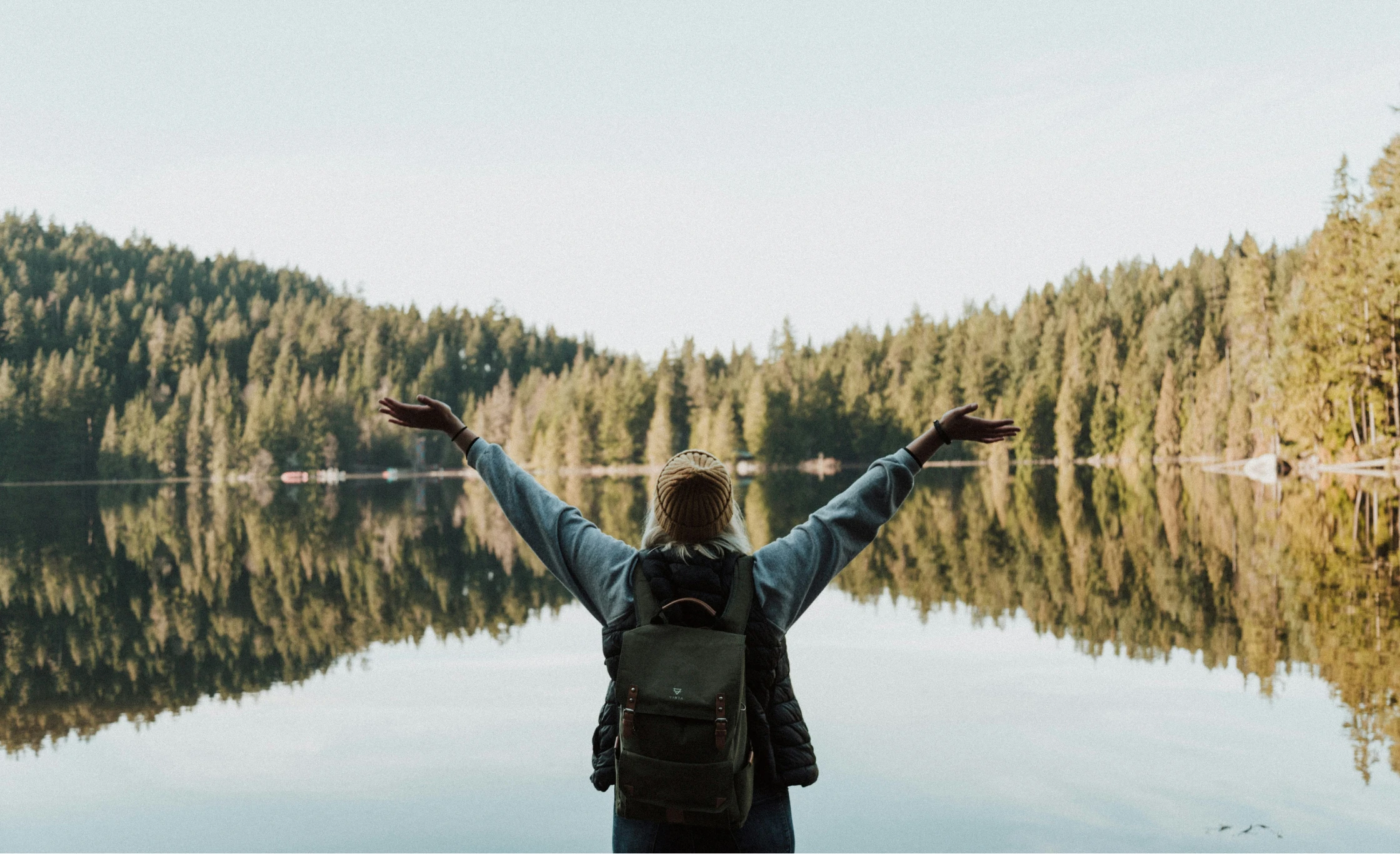 Fri kvinne ute på tur ser over innsjø i skog
