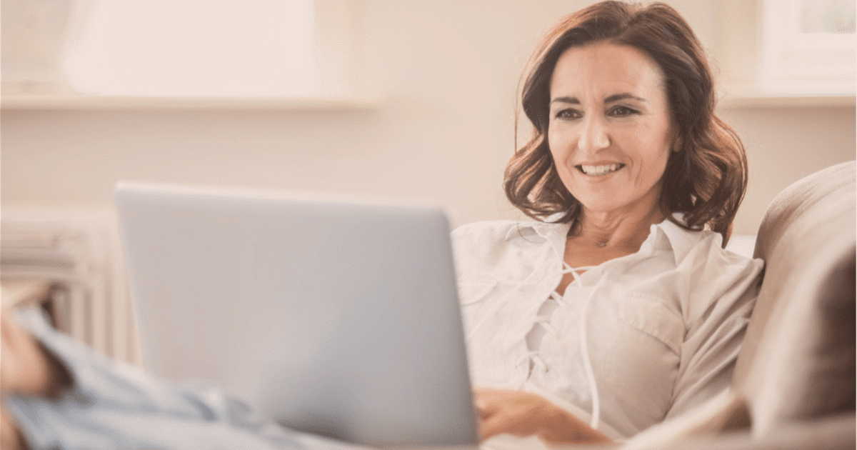 smilende kvinne sitter foran pc