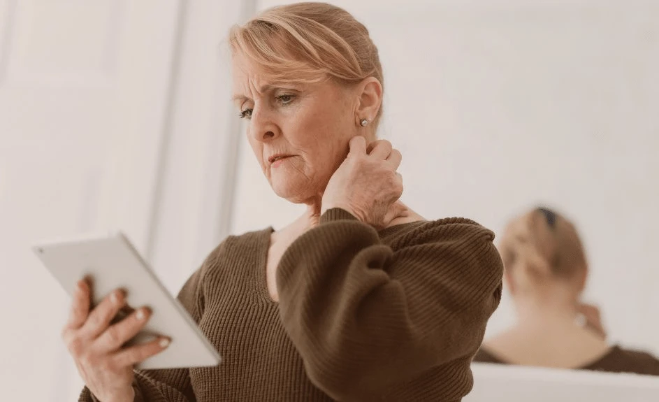 Dame ser bekymret på nettbrett og holder seg for nakken