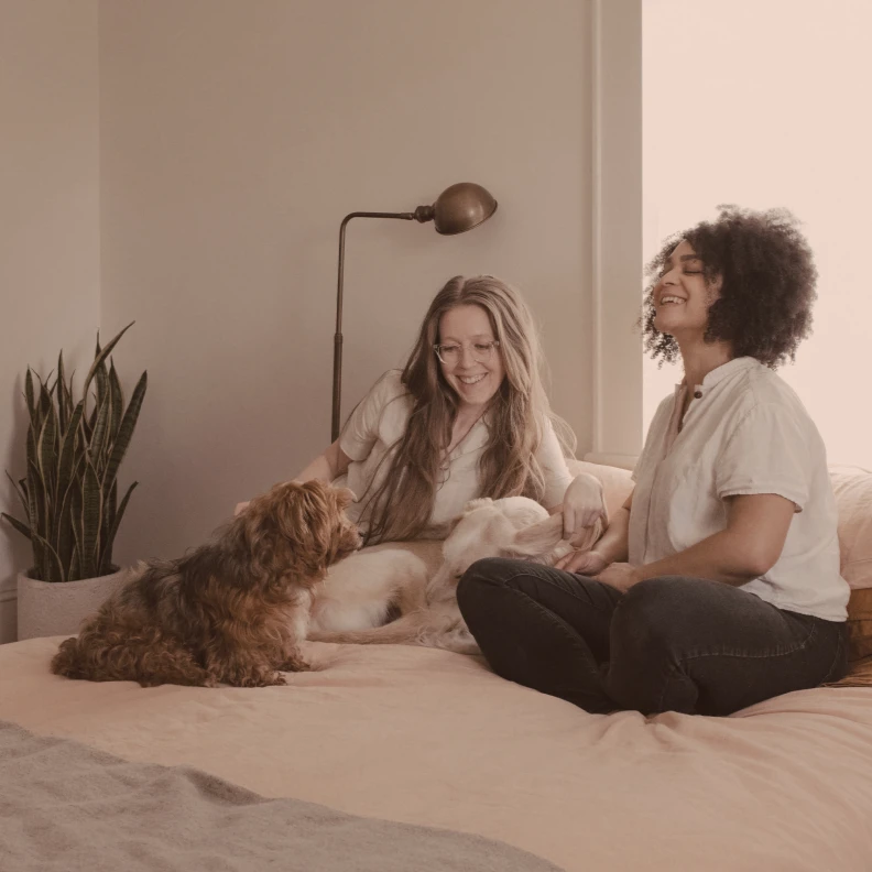 smilende jentevenner og hund på seng